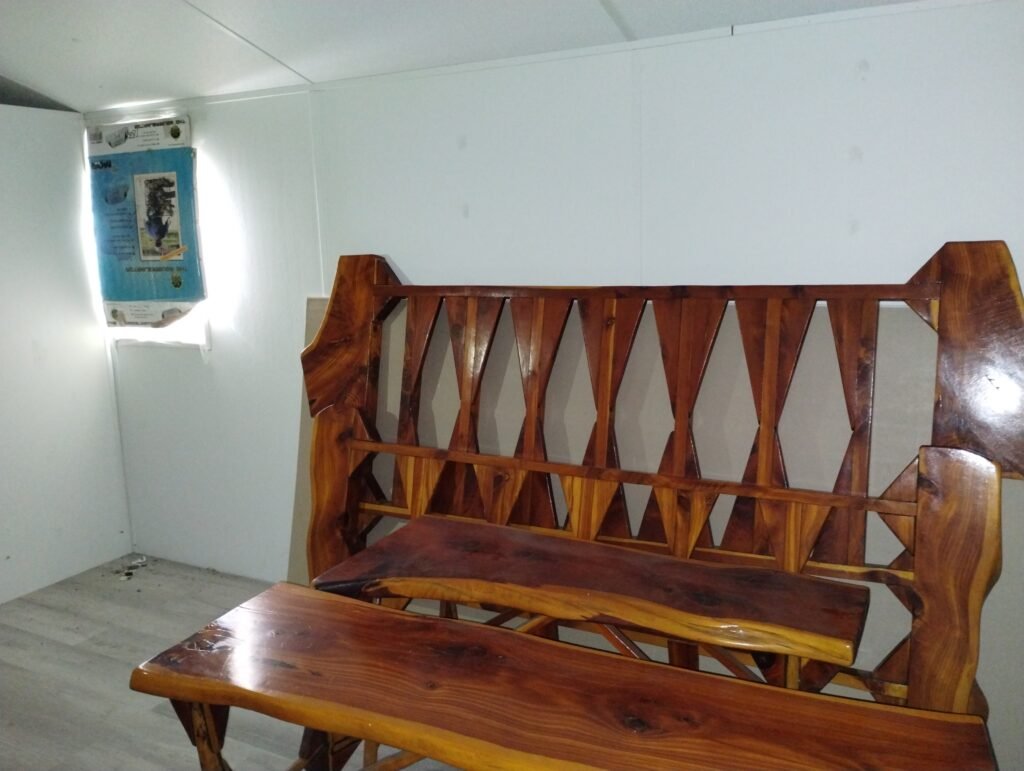 view of the outside wall of the bedroom,  a cardboard covered window to the left, a cedar headboard is leaning against the wall with a cedar bench in front of it